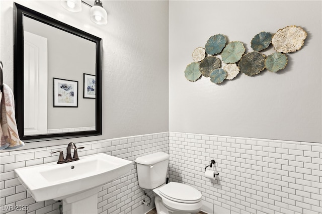 half bathroom with toilet, a wainscoted wall, tile walls, and a sink