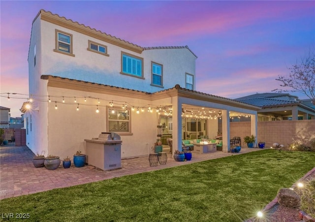 back of property at dusk featuring a patio, a lawn, fence, and stucco siding