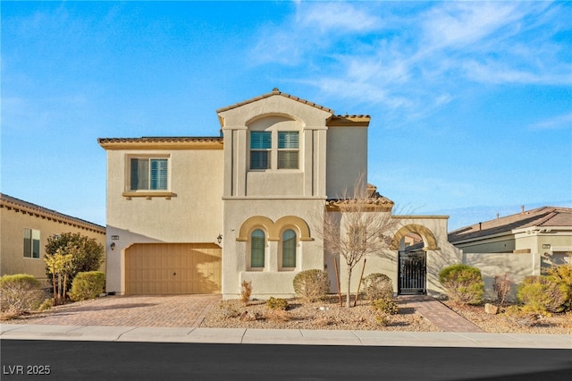 mediterranean / spanish home featuring a garage, a gate, decorative driveway, and stucco siding