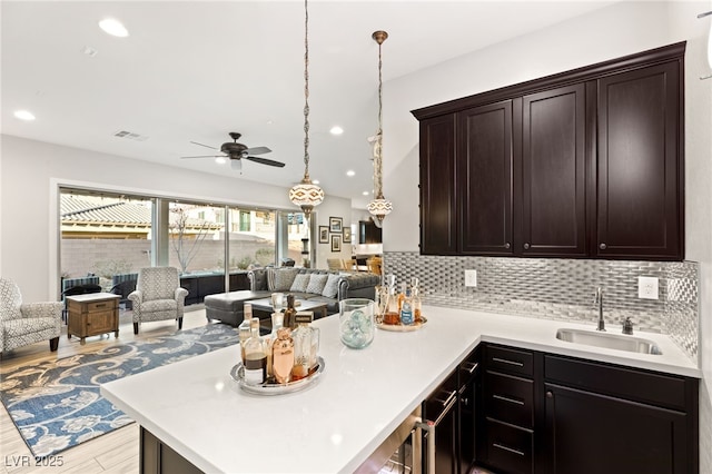 kitchen featuring tasteful backsplash, open floor plan, a peninsula, light countertops, and a sink