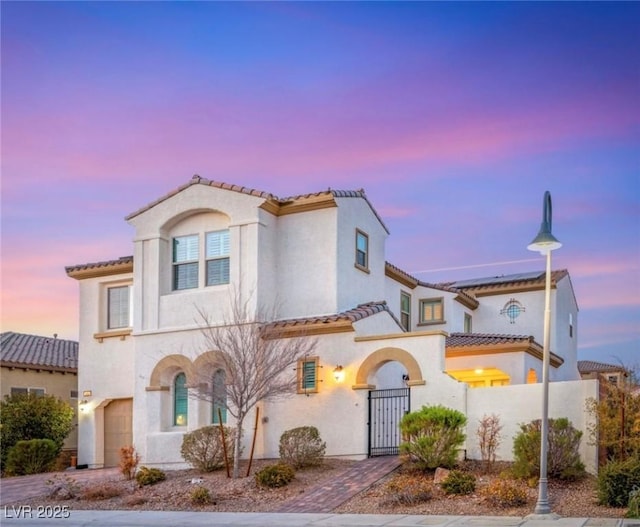 mediterranean / spanish-style home with a garage, a gate, fence, and stucco siding