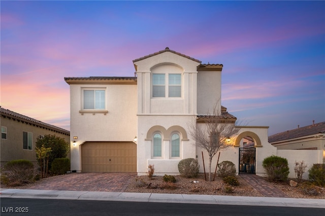 mediterranean / spanish home with a garage, a tiled roof, decorative driveway, and stucco siding