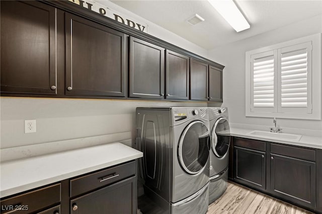 laundry area featuring cabinet space, a sink, light wood-style flooring, and separate washer and dryer