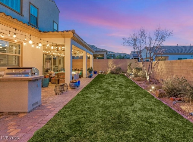 yard at dusk featuring exterior kitchen, a fenced backyard, and a patio