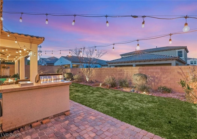 patio terrace at dusk with a fenced backyard, a lawn, and area for grilling