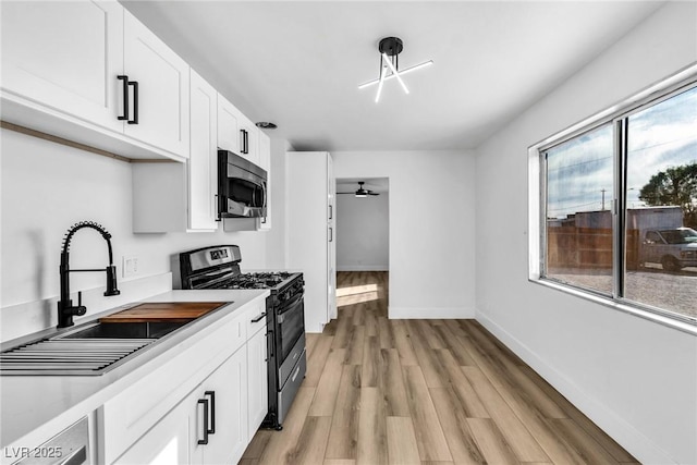 kitchen with white cabinets, stainless steel appliances, light countertops, light wood-style floors, and a sink