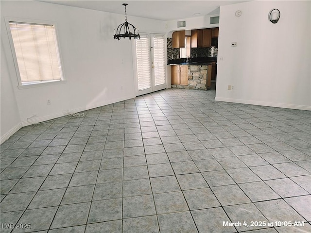 unfurnished living room with light tile patterned floors, baseboards, a sink, and an inviting chandelier