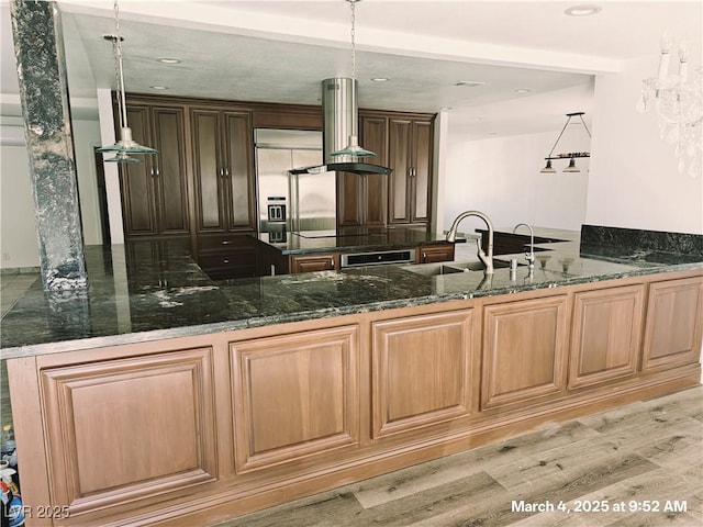 kitchen with wall oven, dark stone counters, a peninsula, island exhaust hood, and a sink