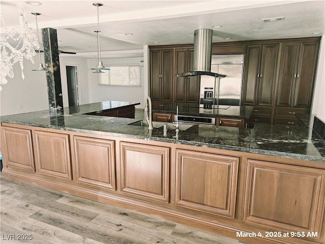 kitchen with light wood-style floors, island exhaust hood, dark stone counters, and decorative light fixtures