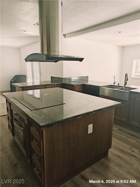 kitchen featuring a textured ceiling, black electric cooktop, island range hood, a sink, and dark wood finished floors