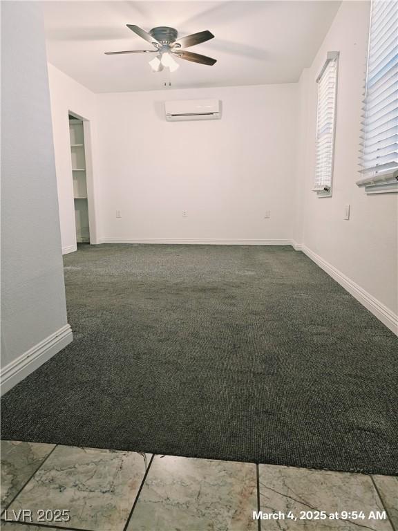 spare room featuring carpet floors, a wall unit AC, a ceiling fan, and baseboards