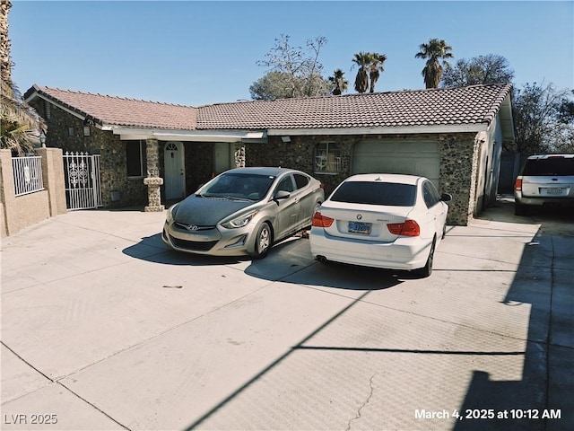 ranch-style home featuring an attached garage, fence, stone siding, driveway, and a tiled roof