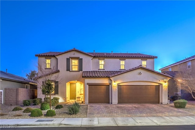 mediterranean / spanish home featuring a tile roof, fence, decorative driveway, and stucco siding