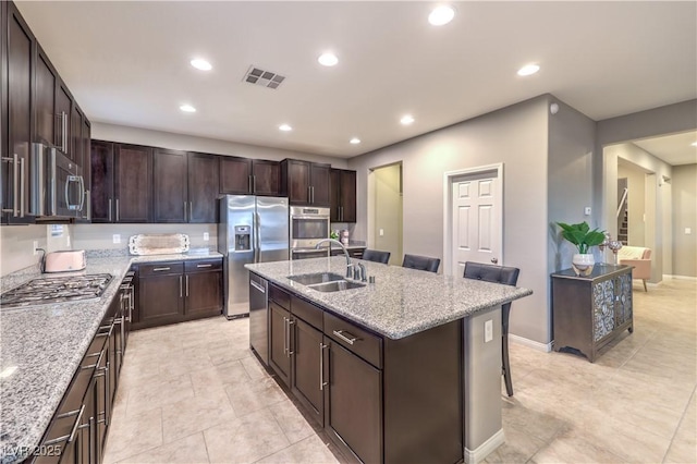 kitchen with visible vents, a kitchen breakfast bar, light stone countertops, stainless steel appliances, and a sink