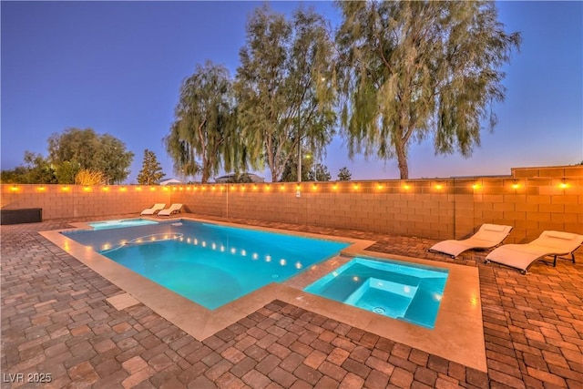 pool at dusk featuring a patio area, a fenced backyard, and an in ground hot tub