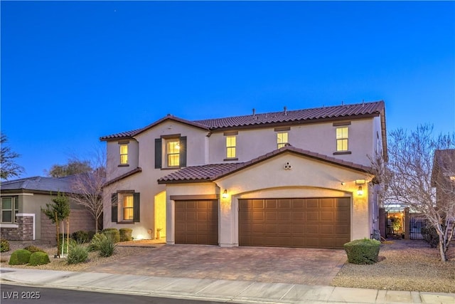 mediterranean / spanish-style home featuring decorative driveway, a tile roof, stucco siding, fence, and a garage