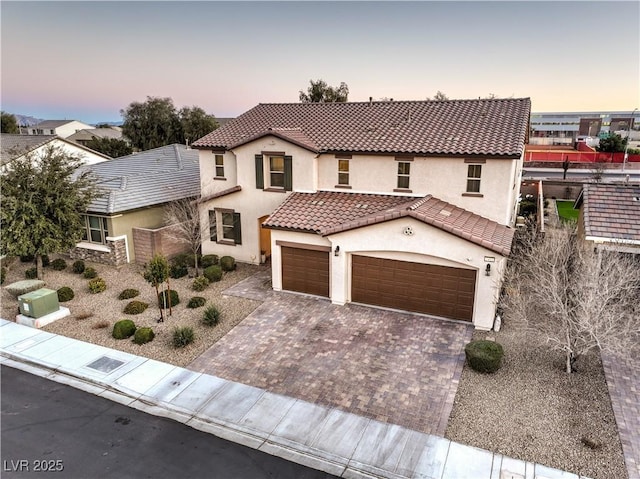 mediterranean / spanish-style house with decorative driveway, a tiled roof, an attached garage, and stucco siding