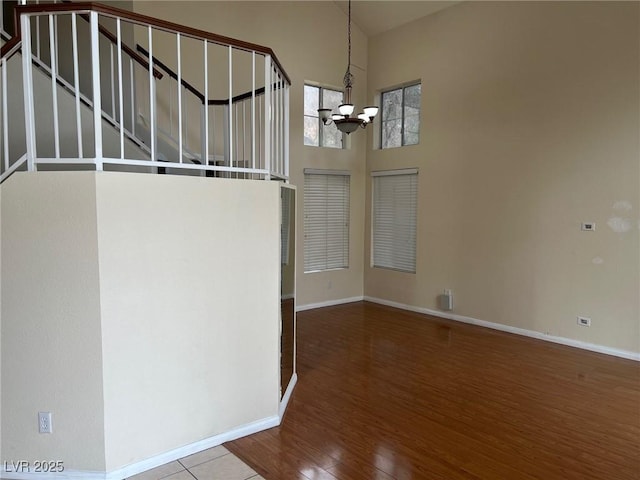 interior space with baseboards, a towering ceiling, stairway, wood finished floors, and a notable chandelier