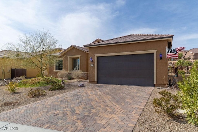 view of front facade with decorative driveway, a tile roof, an attached garage, and stucco siding