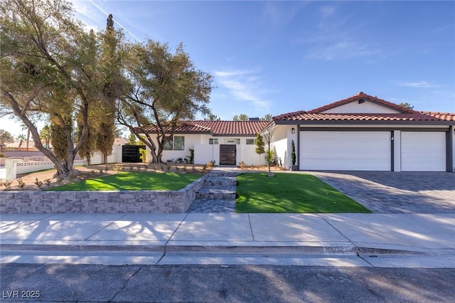 mediterranean / spanish-style house with decorative driveway, stucco siding, an attached garage, a front yard, and a tiled roof