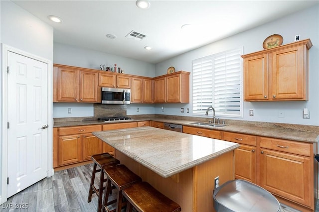 kitchen with a sink, visible vents, appliances with stainless steel finishes, a center island, and a kitchen bar