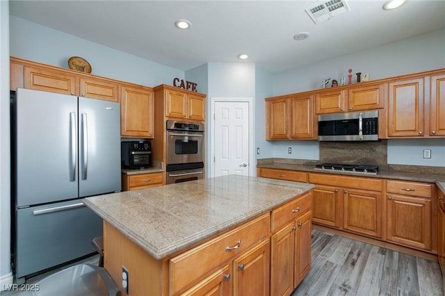 kitchen featuring light stone counters, stainless steel appliances, visible vents, light wood-type flooring, and a center island