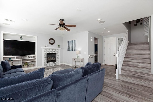 living area featuring baseboards, visible vents, wood finished floors, stairs, and a fireplace