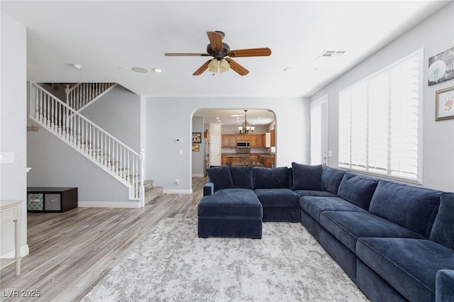 living area featuring arched walkways, wood finished floors, visible vents, baseboards, and stairway