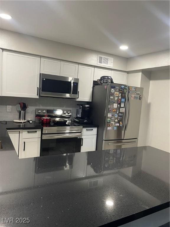 kitchen featuring stainless steel appliances, visible vents, white cabinets, decorative backsplash, and dark stone countertops