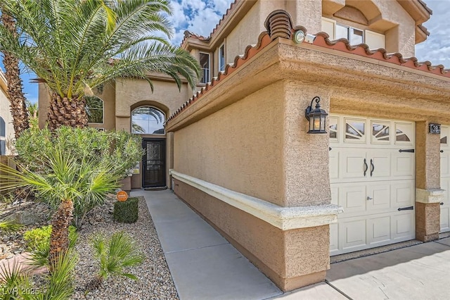 doorway to property with a garage, a tiled roof, and stucco siding