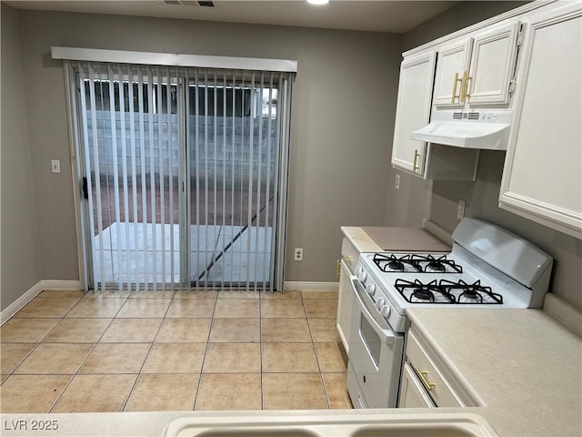 kitchen featuring white gas range, light countertops, under cabinet range hood, white cabinetry, and light tile patterned flooring