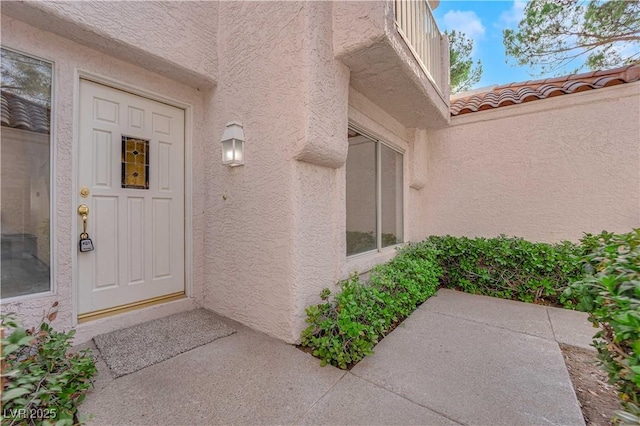 view of exterior entry with a tile roof and stucco siding