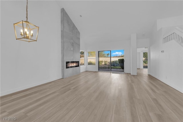 unfurnished living room featuring high vaulted ceiling, baseboards, light wood-style floors, a tiled fireplace, and an inviting chandelier