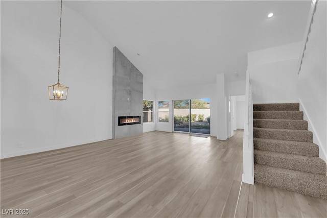 unfurnished living room featuring light wood-style floors, stairs, a fireplace, and high vaulted ceiling