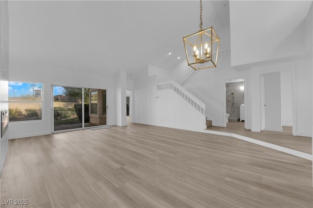 unfurnished living room with a towering ceiling, light wood finished floors, stairs, and an inviting chandelier