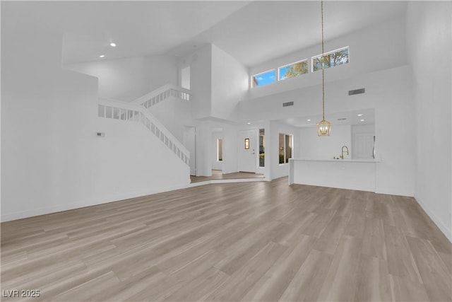 unfurnished living room featuring visible vents, a towering ceiling, light wood-style floors, a chandelier, and stairs