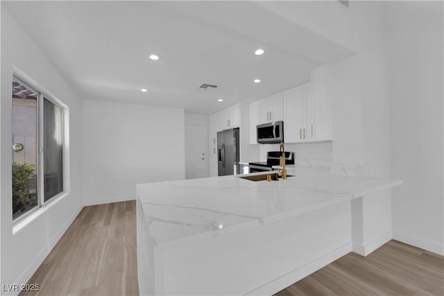 kitchen featuring light wood finished floors, white cabinets, light stone counters, a peninsula, and stainless steel appliances