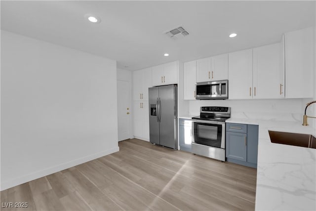 kitchen with light wood finished floors, stainless steel appliances, visible vents, a sink, and light stone countertops