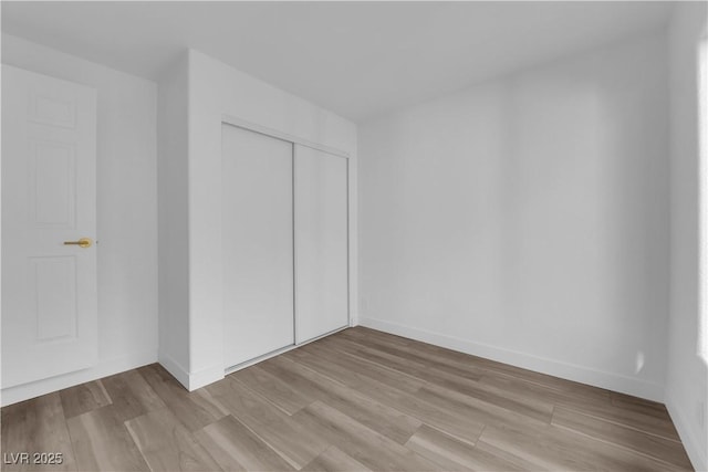 unfurnished bedroom with light wood-type flooring, a closet, and baseboards