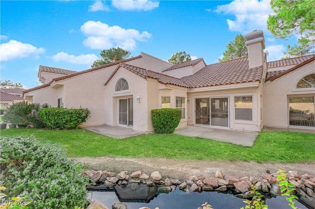 rear view of house featuring a lawn, a patio, a chimney, a tiled roof, and stucco siding