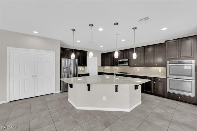 kitchen with stainless steel appliances, visible vents, decorative backsplash, dark brown cabinetry, and a kitchen bar