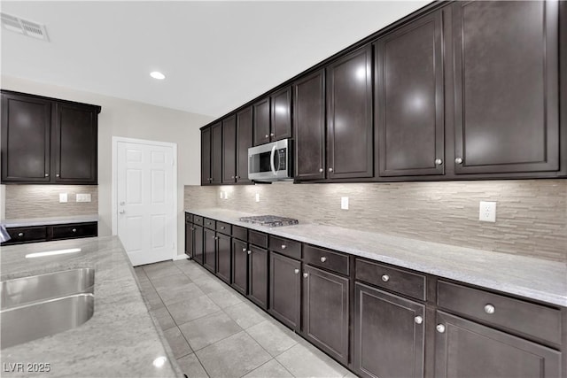 kitchen with dark brown cabinetry, tasteful backsplash, visible vents, stainless steel microwave, and a sink