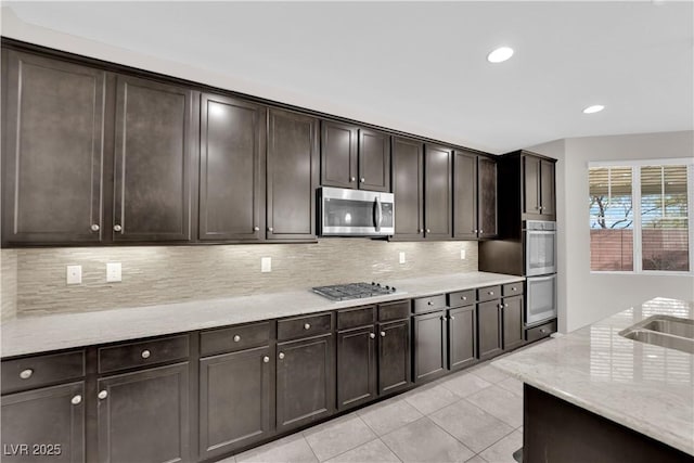 kitchen with light tile patterned floors, dark brown cabinetry, light stone countertops, stainless steel appliances, and decorative backsplash