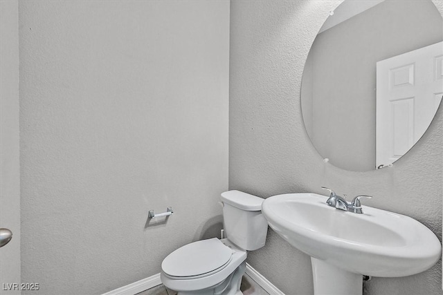 half bathroom with a textured wall, a sink, toilet, and baseboards