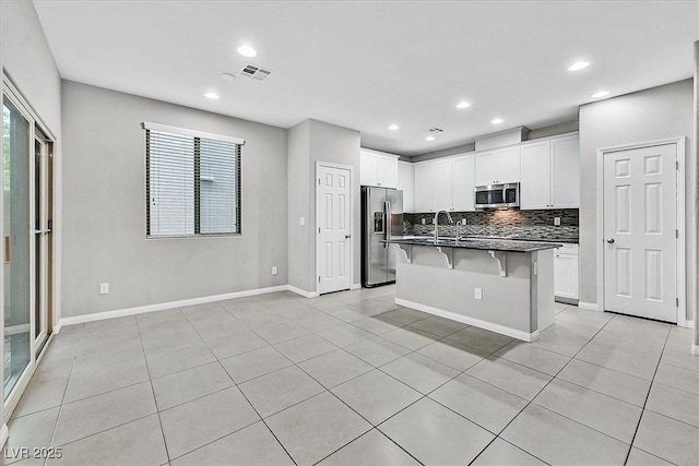 kitchen featuring dark countertops, decorative backsplash, appliances with stainless steel finishes, white cabinets, and a kitchen bar