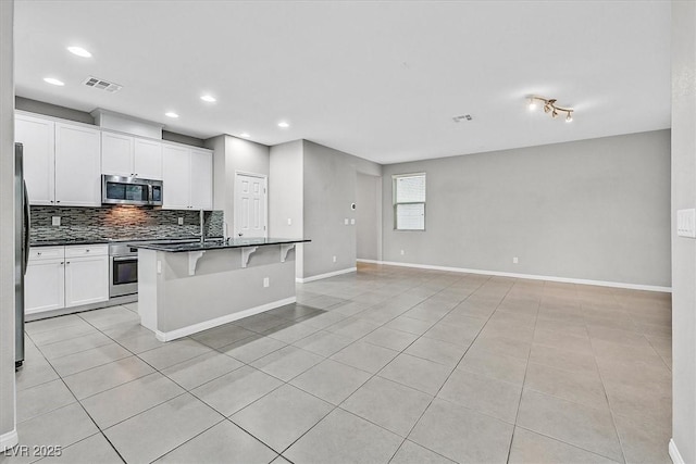 kitchen with visible vents, dark countertops, appliances with stainless steel finishes, open floor plan, and backsplash