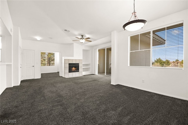 unfurnished living room featuring baseboards, visible vents, a ceiling fan, a fireplace, and dark carpet