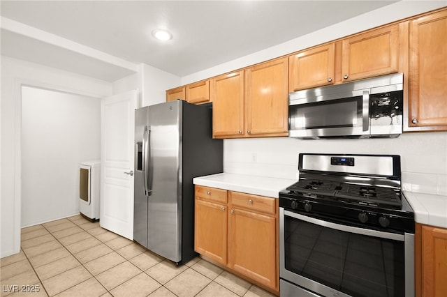 kitchen featuring appliances with stainless steel finishes, tile counters, washer / clothes dryer, and light tile patterned flooring