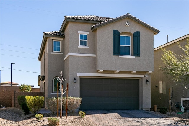 mediterranean / spanish house featuring a garage, a tile roof, fence, decorative driveway, and stucco siding