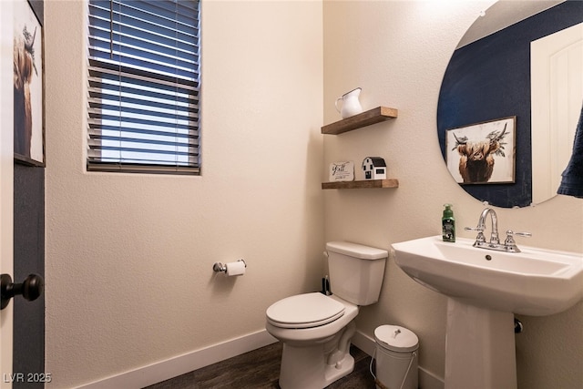 half bath featuring baseboards, a sink, toilet, and wood finished floors